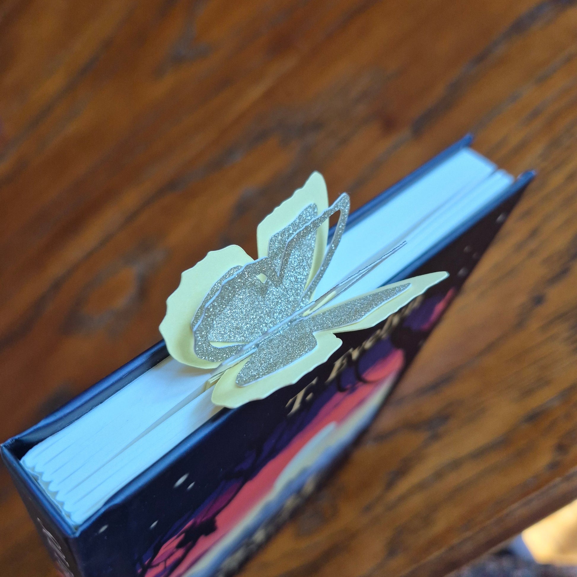 Gult bokmerke i papir med glitter- sommerfugl som bretter ut vingene over toppen av boken.